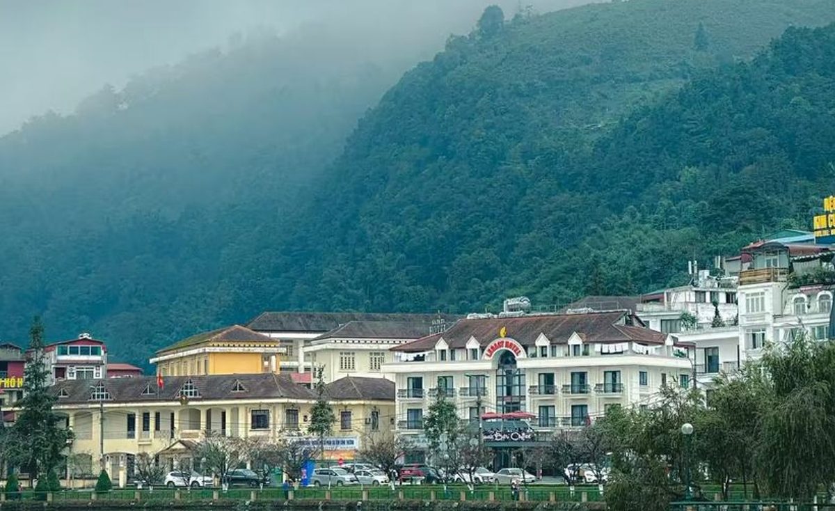 Pekan Sapa di tepi tasik dengan bangunan bergaya kolonial dan gunung hijau berkabus di belakangnya